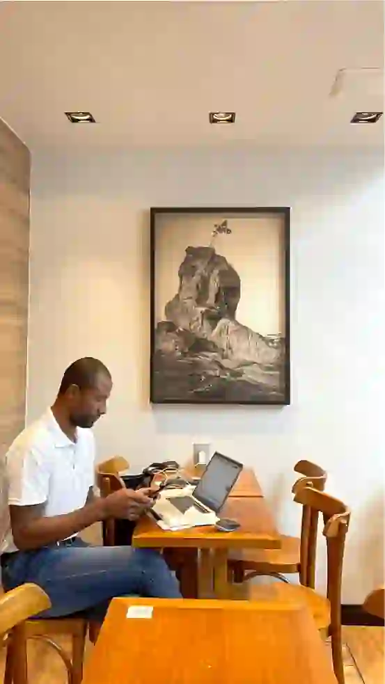 Homem sentado a mesa mexendo em notebook com um quadro ao fundo